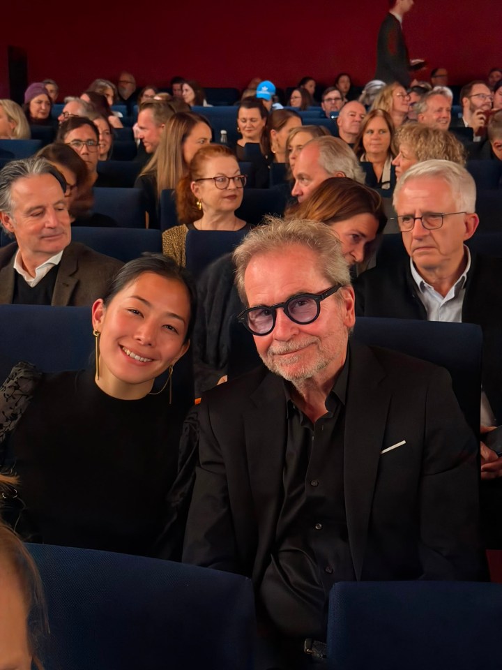 Ein Mann und eine Frau posieren lächelnd in einem Kinosaal mit vielen Zuschauern im Hintergrund.
